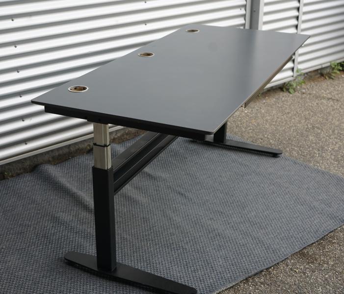 Brugt Duba hæve-sænkebord 180x80 i antracitgrå set fra skrå vinkel, med affasede kanter, kabelbakke og kabelgennemføring.